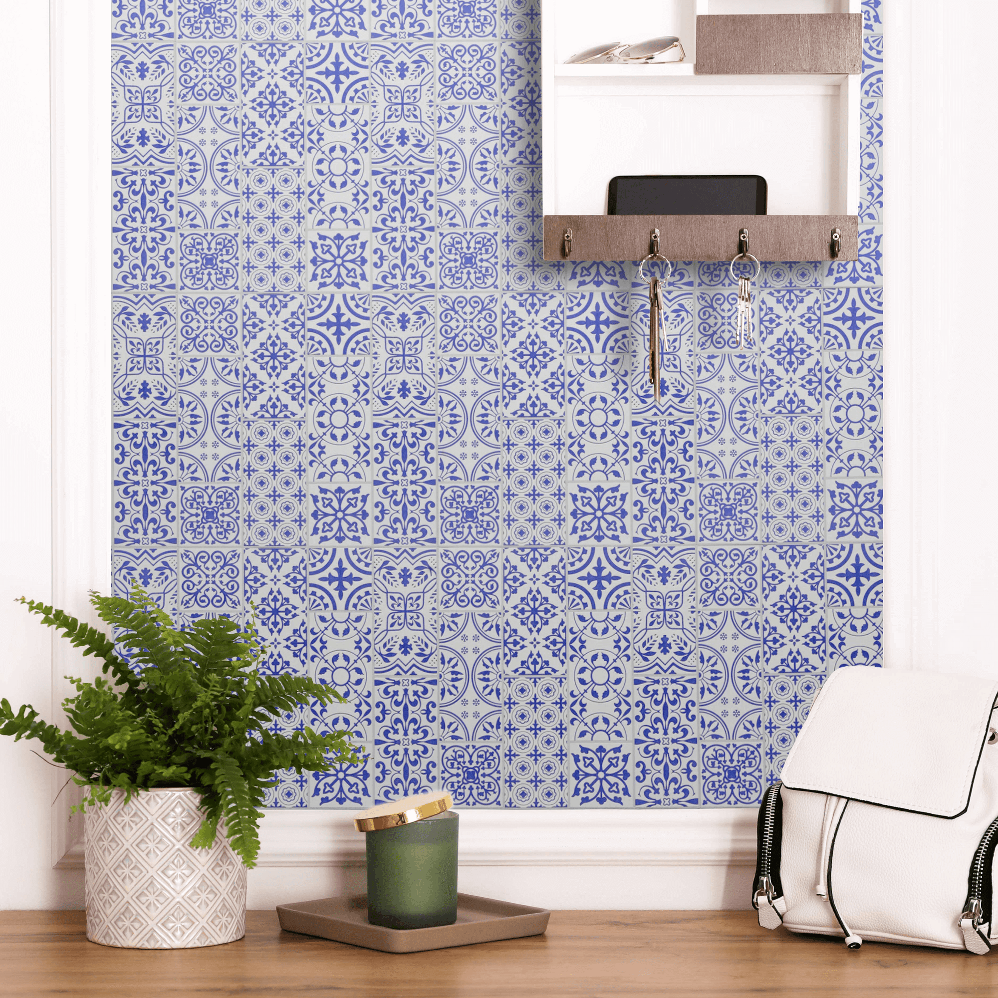 Blue and white peel-and-stick tile pattern brightening a small utility-room wall with a key-hook rail, a potted fern, and a backpack