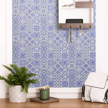 Blue and white peel-and-stick tile pattern brightening a small utility-room wall with a key-hook rail, a potted fern, and a backpack