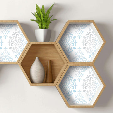 Four hexagon wall shelves in light wood, three of them backed with pale blue and gray patterned paper and one left bare, holding a fern, a vase and a small wooden object.