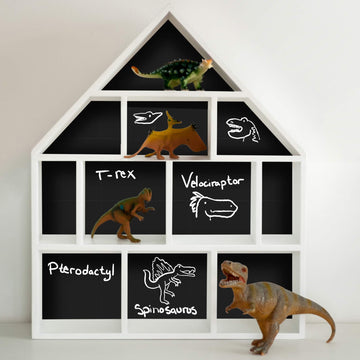 White house-shaped display shelf with chalkboard paper lining the back of each compartment, dinosaur names written in chalk beside toy dinosaurs