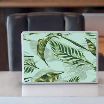 A closed silver laptop standing upright on a white counter, its lid fully covered with green palm leaf self-adhesive paper.
