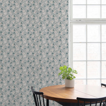 Round wooden dining table with black spindle-back chairs and a potted plant in a ribbed white pot, set against a blue-gray floral wallpapered wall beside a tall paned window