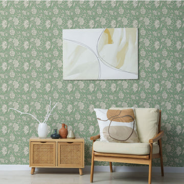 Sage green block-print floral peel and stick wallpaper on a living room accent wall behind a mid-century lounge chair, a cane console, and framed art.