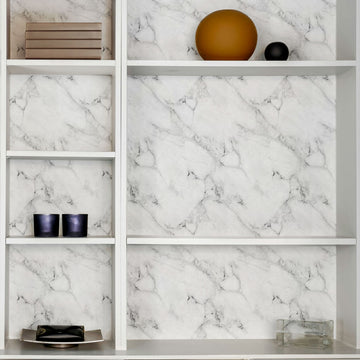 Open shelving backed with Carrara marble peel and stick wallpaper, styled with books, candles and decor — a dry-zone kitchen accent idea.