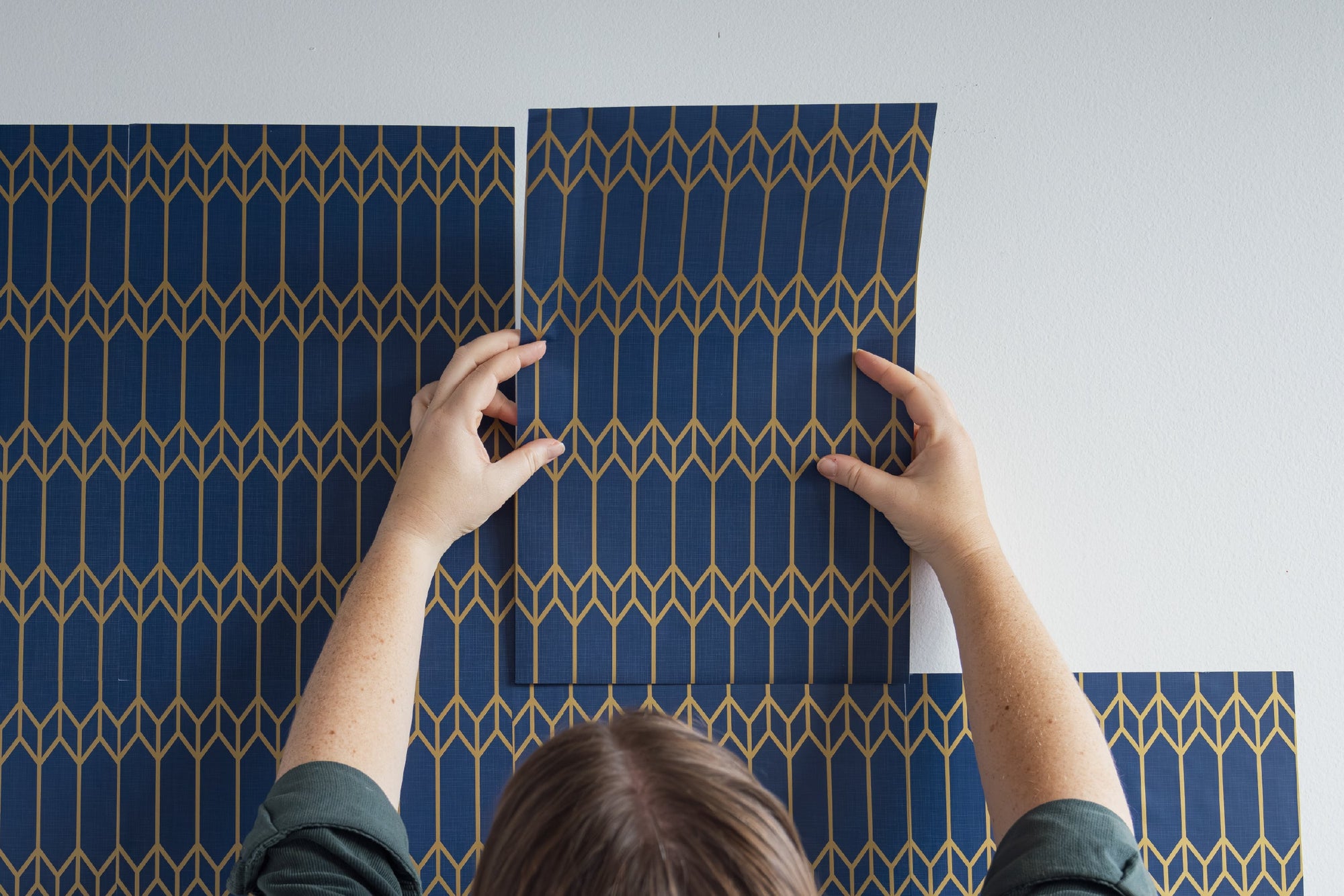 Laying out peel and stick wallpaper sheets across a wall to plan coverage — measuring how many sheets a project needs