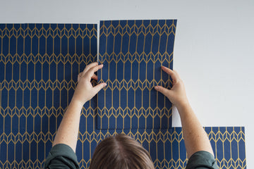 Laying out peel and stick wallpaper sheets across a wall to plan coverage — measuring how many sheets a project needs