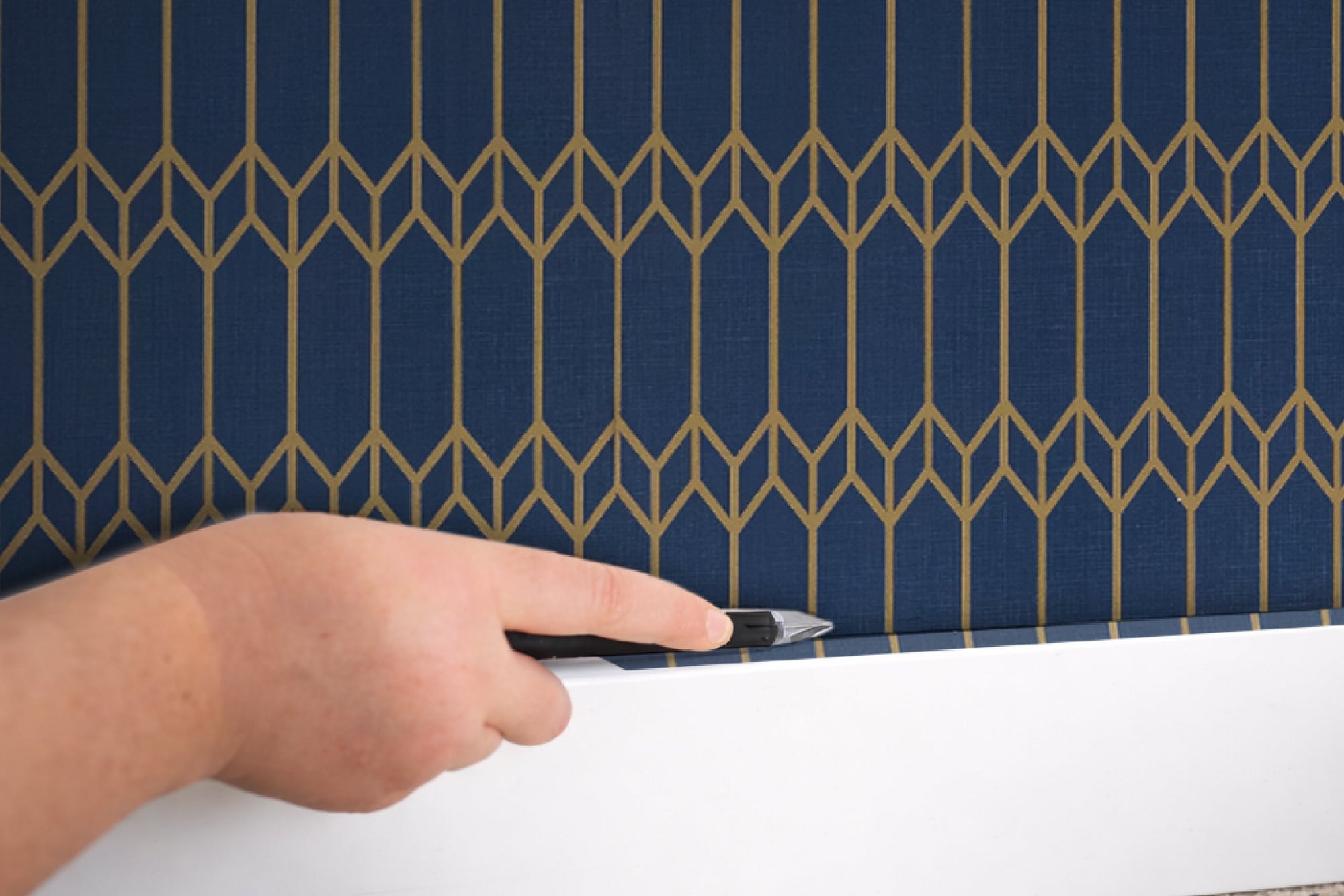 Trimming the bottom edge of installed peel and stick wallpaper with a utility knife along the baseboard — finishing corners cleanly