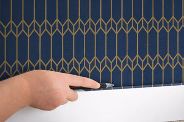 Trimming the bottom edge of installed peel and stick wallpaper with a utility knife along the baseboard — finishing corners cleanly