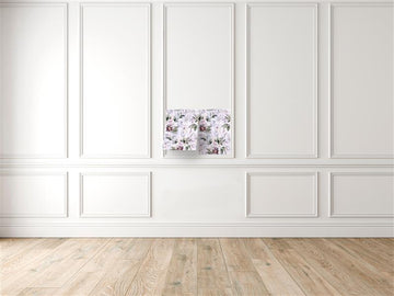 Two floral peel and stick wallpaper sheets in lilac, green and plum tones side by side on a white paneled wall, their lower edges lifting slightly, above a light oak floor