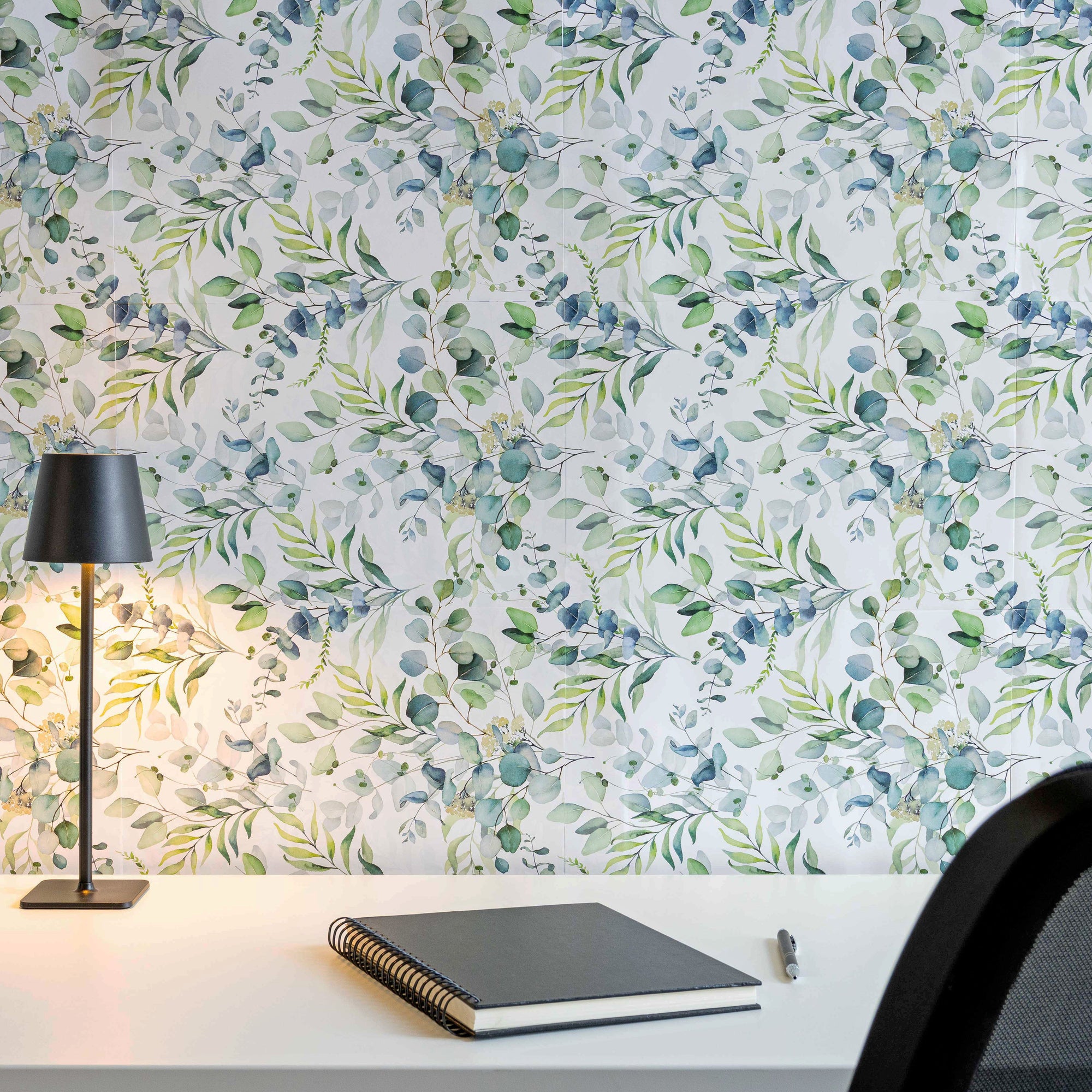 Eucalyptus-patterned peel and stick wallpaper covering an accent wall behind a desk lamp and notebook