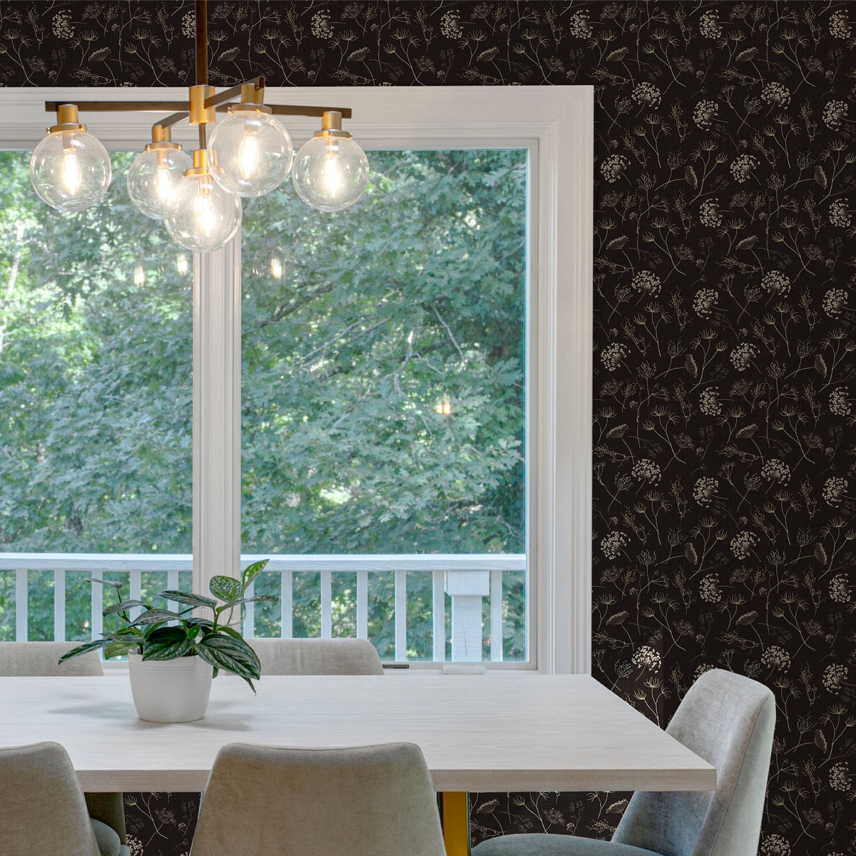 Dining room with a white table, gray upholstered chairs and a brass globe chandelier in front of a large white-framed window, the surrounding wall covered in dark Queen Anne's Lace peel and stick wallpaper with cream wildflowers