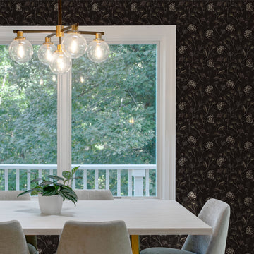 Dining room with a white table, gray upholstered chairs and a brass globe chandelier in front of a large white-framed window, the surrounding wall covered in dark Queen Anne's Lace peel and stick wallpaper with cream wildflowers