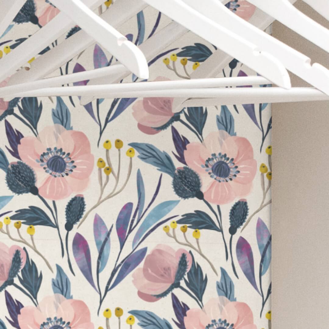 Floral peel and stick wallpaper lining the back wall inside a closet, seen from beneath the shelf, with white hangers on the rod